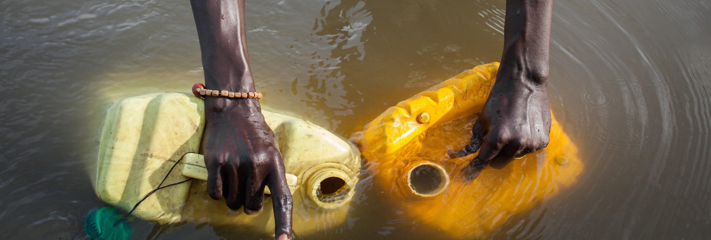 Hands holding bottles filling water in river