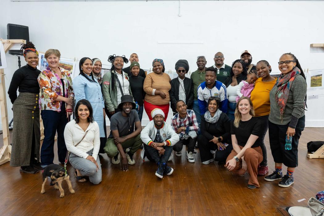 Group picture of 20+ people and one little puppy posing for shot in bright exhibition space