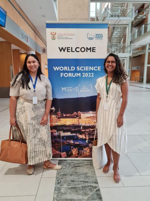 Nadine Veldsman and Imaan Mohamed standing in front of the World Science Forum welcome signage