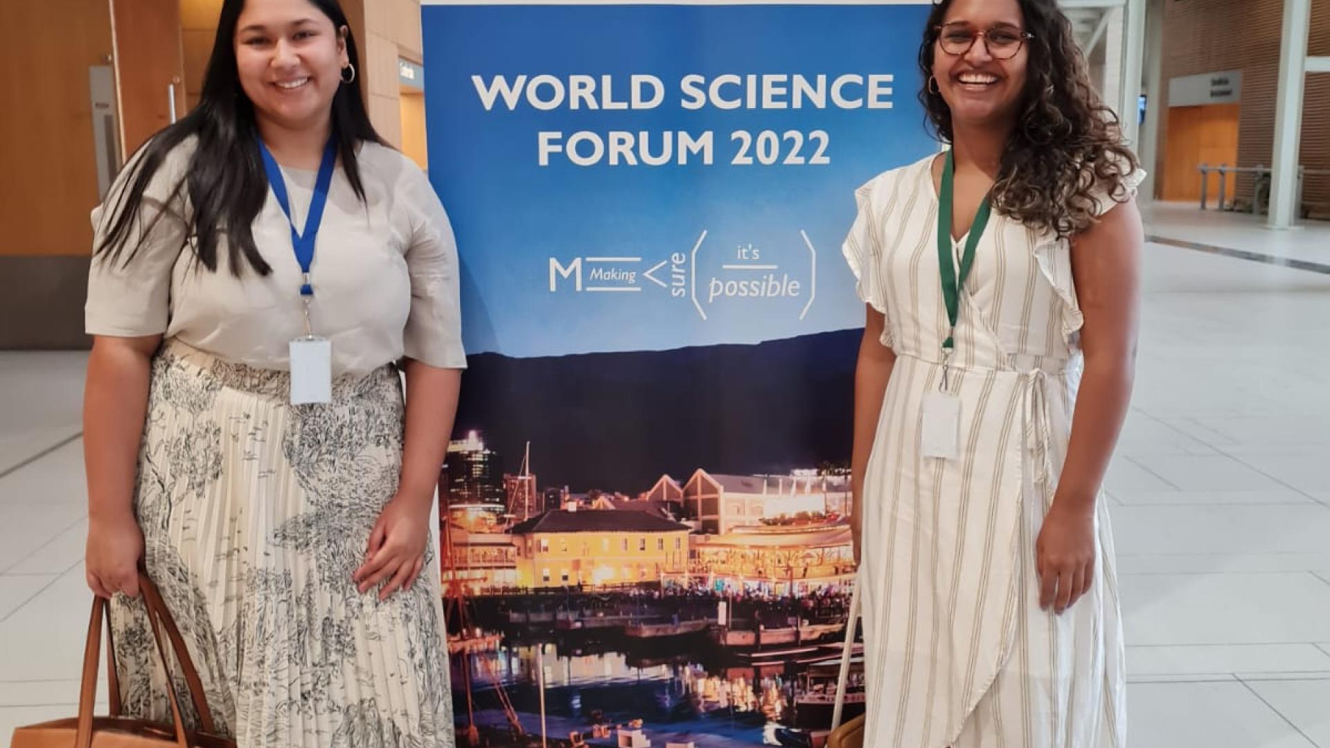 Nadine Veldsman and Imaan Mohamed standing in front of the World Science Forum welcome signage