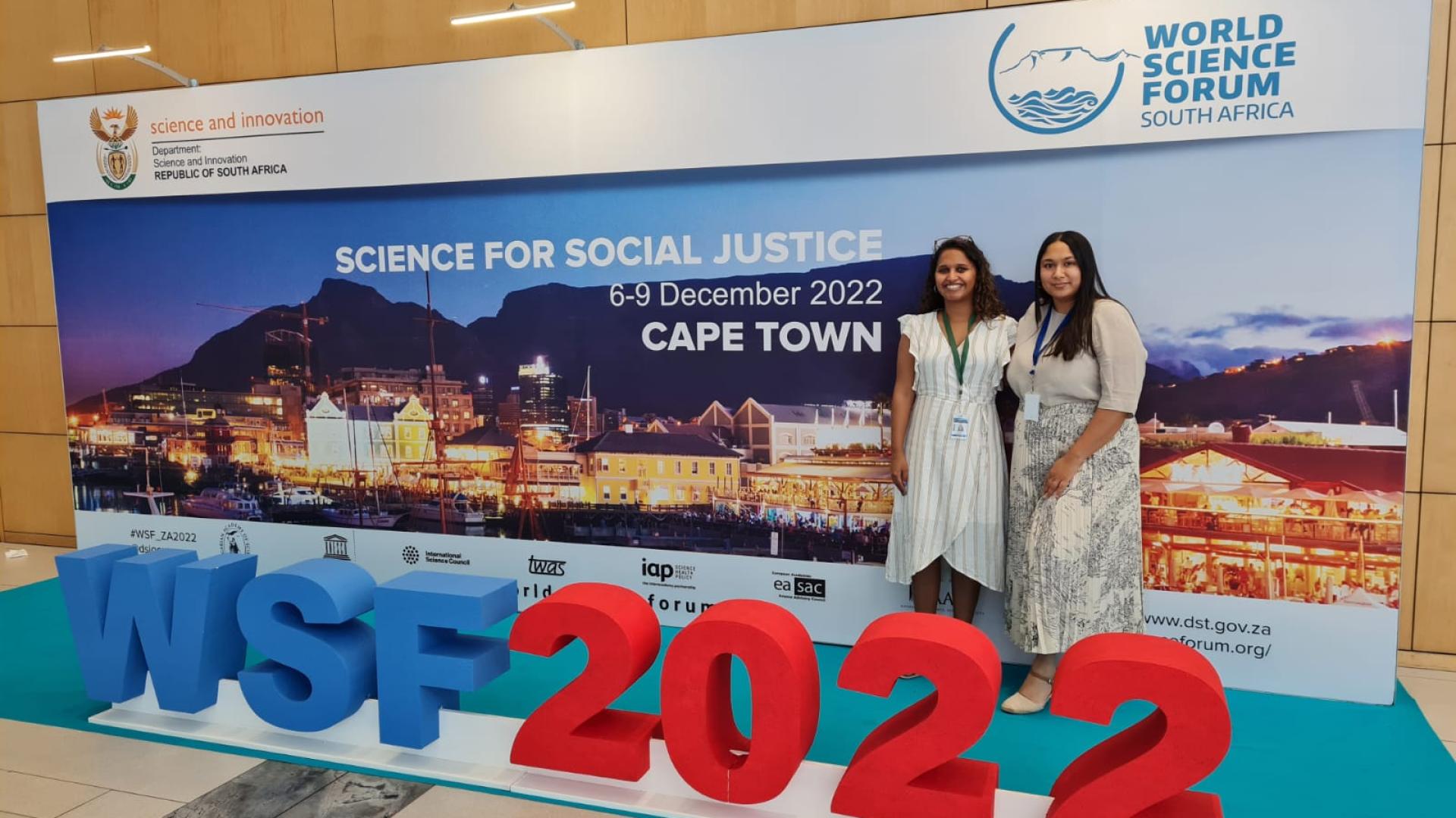 Nadine Veldsman and Imaan Mohamed standing in front of the World Science Forum signage