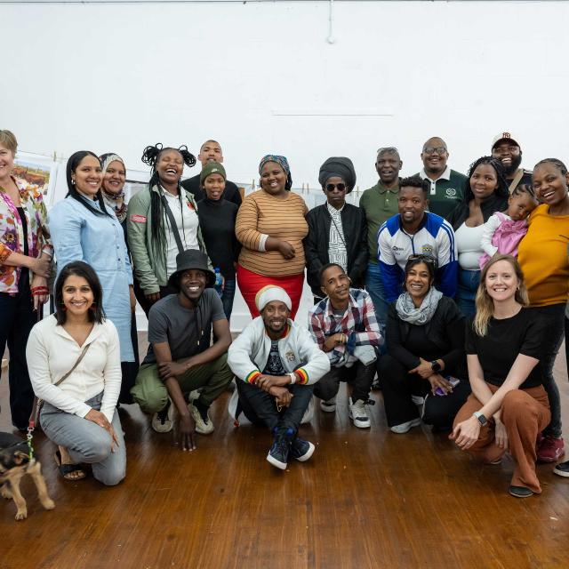 Group picture of 20+ people and one little puppy posing for shot in bright exhibition space