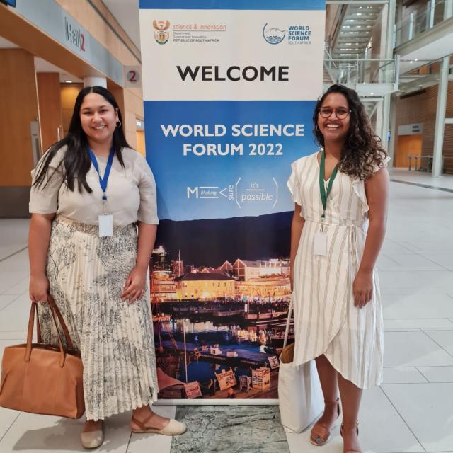 Nadine Veldsman and Imaan Mohamed standing in front of the World Science Forum welcome signage
