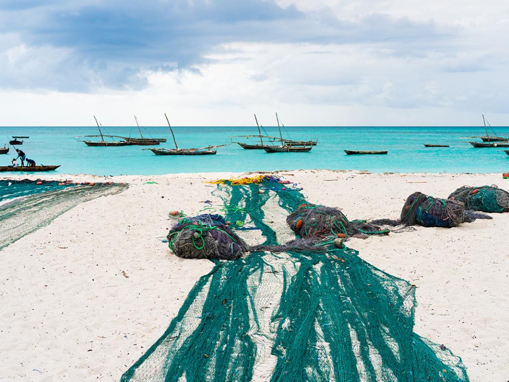 Large fishing nets lying on african beach with boats near the shore